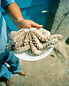 GREECE, Patmos, Diakofti, Dodecanese Island, Kostas holds a plate of octopus at Diakofti Taverna