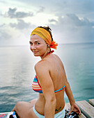 HONDURAS, Roatan, portrait of a young woman sitting on pier at Sunset, Caribbean Sea
