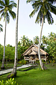 INDONESIA, Mentawai Islands, Kandui Surf Resort, exterior of a guest cabin at Kandui resort with lawn and palm trees