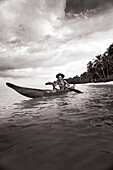 INDONESIA, Mentawai Islands, Kandui Resort, fisherman Gesayas Ges paddling his dugout canoe (B&W)