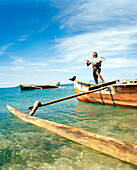 MADAGASCAR, boy holding fish standing on dugout canoe, Nosy Komba