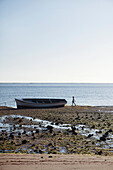MAURITIUS, a young girl walks on the beach by a fishing boat in Bel Ombre