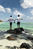 MAURITIUS, twin boys fish side by side off of some rocks, Iles aux Cerfs Island