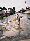PANAMA, Bocas del Toro, a surfer walks through the middle of town in the rain, Central America