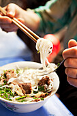 VIETNAM, Hanoi, restaurant Pho Gia Truyen, also known as 49 Bat Dan, a woman eats a bite of pho bo (beef noodle bowl) in the traditional way with a spoon and chopsticks