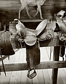 USA, Wyoming, horse saddle on wooden railing, Old Trail Town, Cody (B&W)