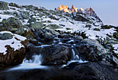Sunrise over the snowy French Alps with mountain stream and the peak of Aiguille de l'Encrenaz in Autumn, Savoy, France