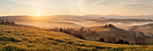 Panorama of a sunrise over the Val d'Orcia near Pienza on a foggy morning in spring, Tuscany, Italy