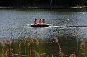 Three children in a rubber boat in Lake Tennsee, Karwendel mountain range near Mittenwald, Bavaria, Germany