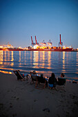 Guests on the beach near Cafe Strandperle in Hamburg-Oevelgoenne, the HHLA container terminal is situated on the opposite bank of the Elbe, Hamburg harbour, Hamburg, Germany