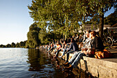 People sitting on the seawall at Alsterperle Cafe and bar, Eduard-Rhein-Ufer 1, Outer Alster Lake, Hamburg, Germany