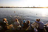 People sitting on seawall at cafe and bar Alsterperle, Eduard-Rhein-Ufer 1, Outer Alster Lake, Hamburg, Germany