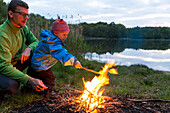 Father and son (2 years) near a campfire at lakeside, near Blumenholz, Mecklenburg-Western Pomerania, Germany