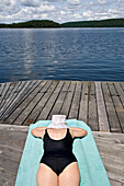 Woman sunbathing on cottage dock, Smoke Lake, Algonquin Park, Ontario