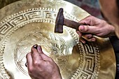 Kingdom of Morocco, Fes, Fes el Bali, Medina of Fes - listed by UNESCO as a world heritage site in 1981, Copper Souk, Craftsman working on copperware, Close up of a hand holding a hammer and a thin graver