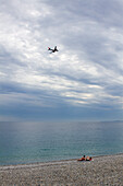 France,  Provence-Alpes-Côte d'Azur, Nice, Couple sunbathing on the beach, air plane crossing the sky