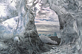 A hole in a coastal iceberg by the atlantic ocean with other icebergs seen through it, iceland