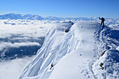 Mountaineer climbing ridge at Birnhorn, with view to snow covered south face of Birnhorn with sea of fog in the valleys, back-country skiing, Birnhorn, Leoganger Steinberge range, Salzburg, Austria