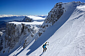 Female backcountry skier ascending through snow-covered cirque at Monte Sirente, Maiella range in background, Valle Lupara, Abruzzo, Italy