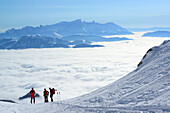 Three persons back-country skiing ascending to Hochkoenig, sea of fog in the valley of Salzach and Dachstein range in the background, Hochkoenig, Berchtesgaden range, Salzburg, Austria