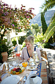 Woman having breakfast on the terrace of a breakfast restaurant, Deia, Majorca, Spain
