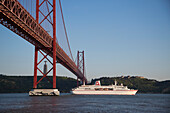 Kreuzfahrtschiff MS Deutschland (Reederei Peter Deilmann) unter der Brücke Ponte 25 de Abril über den Fluss Tejo mit Christusstatue in der Distanz, Lissabon, Portugal