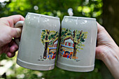 Two beer mugs being clinked together at Entla's Keller beer garden, Erlangen, Franconia, Bavaria, Germany