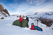 Young couple putting up a tent in snow, Dolomites, Belluno, Veneto, Italy
