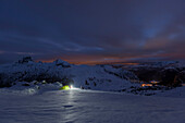 Young woman with headlamp sitting beside a tent in snow, the Dolomites, Belluno, Veneto, Italy