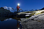 Female hiker with headlamp passing a mountain lake above the Roseg valley, Piz Morteratsch, Piz Bernina and Piz Roseg in background, Engadin, Canton of Grisons, Switzerland