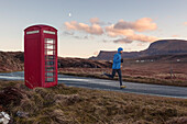 Junger Mann joggt an einer rote Telefonzelle vorbei, Trotternish Halbinsel, Isle of Skye, Schottland, Großbritannien