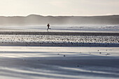 Junge Frau joggt am Strand im Gegenlicht, Dunnet Bay, Caithness, Schottland, Großbritannien