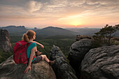Young woman sitting on a rock while enjoying sunset, National Park Saxon Switzerland, Saxony, Germany