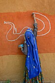 India, Rajasthan, Tonk region, Woman painting clay walls prior to Diwali festival.