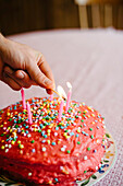 Cake With Pink Icing and Star Sprinkles Being Lit With Candles
