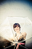Junge Frau lächelt durch einen durchsichtigen Regenschirm