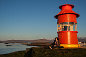 Couple Leaning Against The Stykkisholmur Lighthouse Looking At The Midnight Sun, Snaefellness Peninsula, Western Iceland