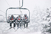 Three Male Skiers Ride A Chairlift In The Snow At Alyeska Ski Resort In Girdwood Alaska