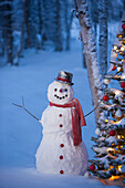 Snowman With Red Scarf And Black Top Hat Standing Next To A Christmas Tree In Snow Covered Birch Forest, Winter