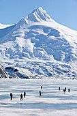A Group Of Skiers Ski Across Frozen Portage Lake With Mount Bard In The Background, Southcentral Alaska, Spring