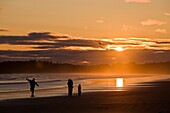 A family playing with a kite under the sunset on the Long Beach of Pacific Rim National Park. Vancouver Island, British Columbia, Canada.