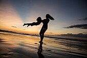 Woman swinging her daughter on the beach at sunset, Costa Rica