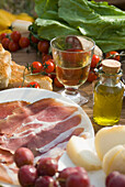 Prosciutto Ham, Cheese, Tomatoes, White Wine And Other Ingredients For A Picnic In Tuscany, Italy.