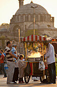 Sweet corn seller in square beside Egyptian Bazaar with Suleymaniye Mosque behind at dusk, Istanbul, Turkey