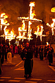 People dressed as monks from Southover Bonfire Society walking in procession down street carrying burning crosses to commemorate 17 protestant martyrs burnt at stake, Lewes, East Sussex, England, UK