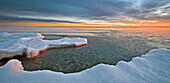 A Fragile Ice Ledge Sits Over A Calm Lake At Sunrise