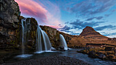 Small waterfall with Kirkjufell in the distance and clouds lit by the rising sun, Snaefellsnes Peninsula, Iceland