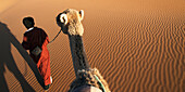 A man leads his camel over the Erg Chegaga Dunes, Morocco