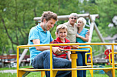 Fahter and son (7 years) at playground, grandparents in background, Styria, Austria