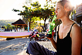 Frau trinkt ein Bier am Strand, Padang Bai, Bali, Indonesien